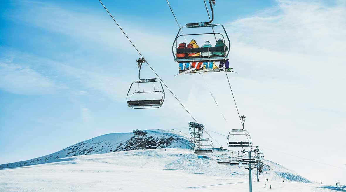 ski lift heading up into the snowy mountains with four skiiers in colourful ski wear sitting on one of the lifts